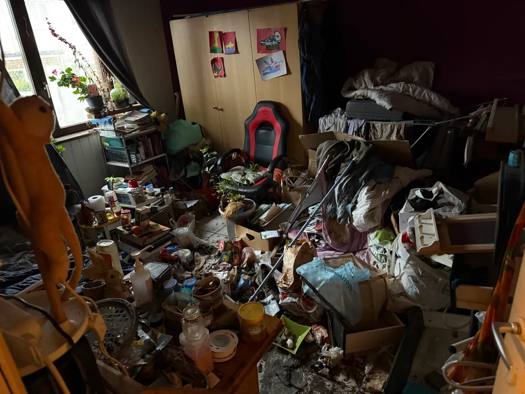 Chambre entièrement encombrée avant intervention, sol invisible sous les objets et les cartons