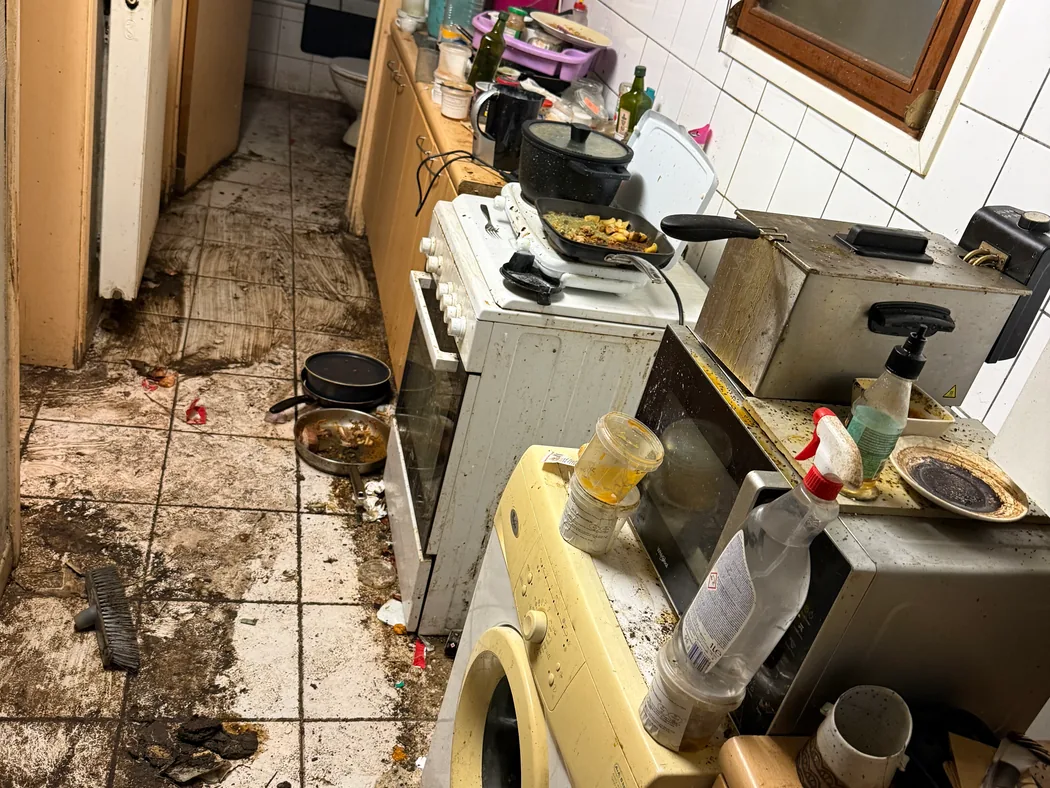 Cuisine avant intervention, plans de travail encombrés et sol recouvert de déchets