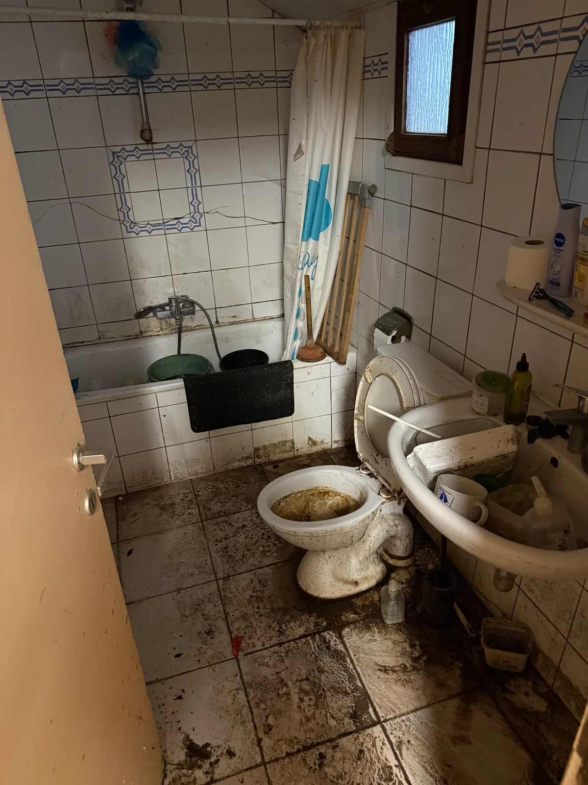 Salle de bain avant notre intervention : sol et sanitaires fortement encrassés, objets entassés dans la baignoire