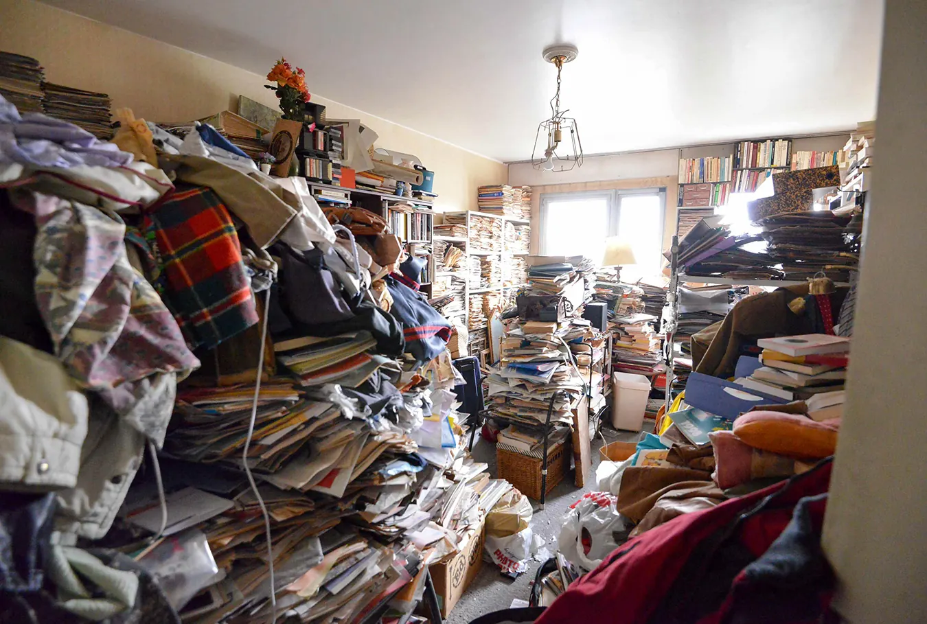 Séjour d'un logement en accumulation sévère, piles de papiers et de vêtements du sol au plafond